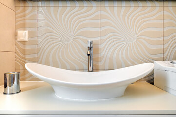 Stylish white ceramic vessel sink with chrome faucet on countertop, set against beige wavy-pattern tiled backsplash. Clean, modern bathroom with elegant and artistic touch.
