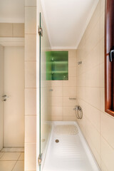 Modern bathroom featuring clean white bathtub, beige tile walls, wall-mounted shower fixtures, glass partition, and small window for natural light. Minimalist and practical interior design.