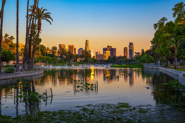 Fototapeta premium Sunset view of downtown Los Angeles skyline from Echo Park Lake with palm trees and paddle boats on the water.
