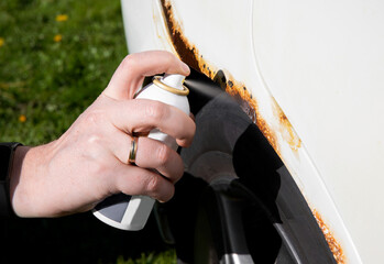 Detail view of person hand apply home use car spray rust stop converter liquid on vehicle rusty...