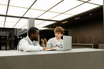 Male intern and male employee sitting at a table and looking at each other, in a hall