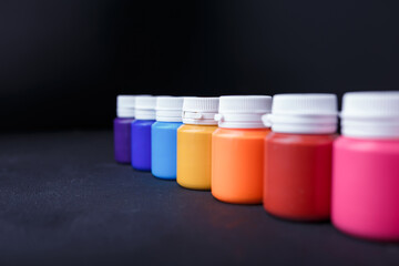 Small bottles of multicolored acrylic or gouache paint jars in a box on dark background. Art materials. Copy space