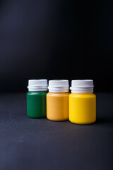 Small bottles of yellow, ochre and green acrylic or gouache paint jars in a box on dark background. Multicolored art materials. Copy space