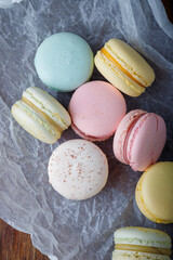 Tender multicolored macaroons with different flavors on paper, wooden rustic background. Top view, closeup shot