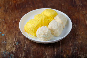 Pismaniye, cotton candy or dragons beard with vanilla and melon taste on white plate, wooden background. Turkish dessert, light halva, candy floss. Copy space