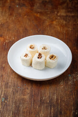 Turkish delight, white locum roll with walnut and coconut flakes on white plate, wooden background. Eastern sweets, oriental food. Traditional tasty dessert. Copy space. Top view