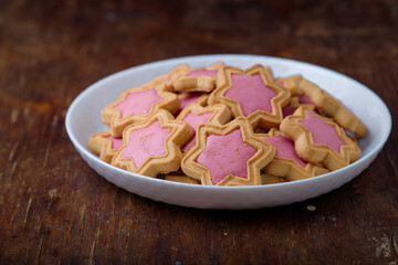 Star shaped cookies with pink frosting on white plate, wooden rustic background. Strawberry icing on cookies in shape of stars. Closeup