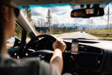 Tourist driving car and using smartphone for navigation while traveling on sunny day towards High Tatras mountain range in Poland. Driver navigating via smartphone while traveling sunny roadway