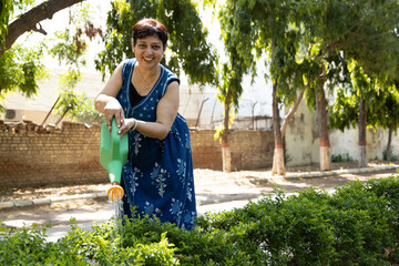 Indian matured woman watering to small plants in garden