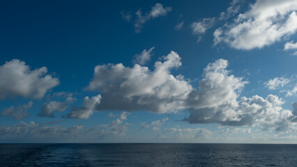Dramatic sky over the ocean. Beautiful blue sky with fluffy white clouds reflecting on calm water. Serene seascape