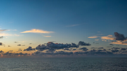 Dramatic twilight sky over the ocean. Dark tones contrast with soft clouds and shimmering water, creating a moody seascape
