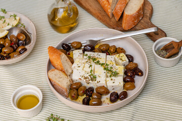 Freshly prepared feta cheese served on a plate with assorted olives, garnished with herbs and lemon slices and crusty bread, traditional Greek or Italian food, Mediterranean diet