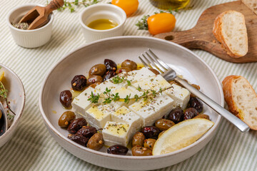 Freshly prepared feta cheese served on a plate with assorted olives, garnished with herbs and lemon slices and crusty bread, traditional Greek or Italian food, Mediterranean diet