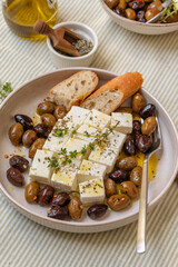 Freshly prepared feta cheese served on a plate with assorted olives, garnished with herbs and lemon slices and crusty bread, traditional Greek or Italian food, Mediterranean diet