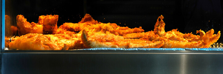 Panorama of fried battered fish in a warming oven at a fish and chip shop