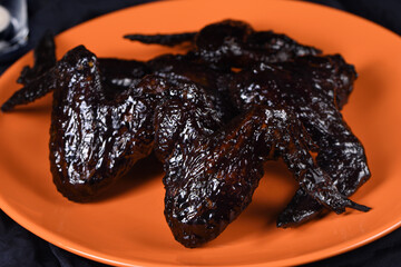 Bat wings. Cooked in sweet and sour sauce with cuttlefish ink, served with ketchup on a plate. An...