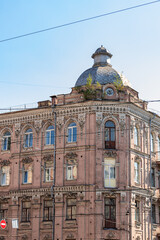 Historic brick building with detailed windows and a silver dome, plants growing on the roof.
