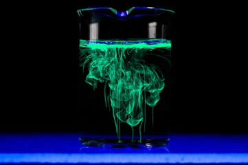 Dissolution and spread of a green substance in a flask with a clear liquid.