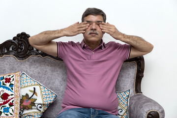 Indian senior Man Rubbing Tired Eyes Having Poor Eyesight Sitting On Couch At Home. Ophthalmology...