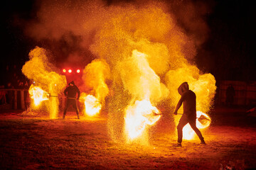 Obraz premium Silhouette of two fire performers with sparkling fire staff erupting in night sky, showcasing energy and artistry of fire manipulation during an outdoor fire show