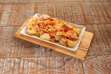 A plate of food with potatoes and cheese on top. The plate is on a wooden board