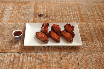 A plate of chicken wings with dipping sauce. The sauce is in a cup. The plate is on a wooden table