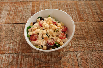A white bowl of salad with tomatoes and croutons. The bowl is on a wooden table