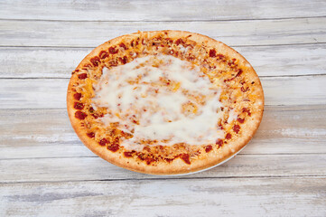 A pizza with cheese and tomato sauce on top. The pizza is on a white plate. The plate is on a wooden table
