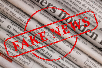 Red Fake News stamp and newspapers in different languages as background, closeup