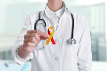 World Hepatitis Day. Doctor with yellow-red awareness ribbon on blurred background, closeup