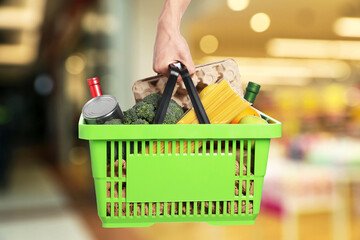 Man holding shopping basket with different food products at supermarket, closeup