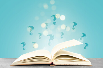Question marks above open book on table against light blue background with blurred lights