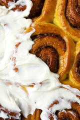 Close up of baked cinnabons with golden crust partially smeared with cream cheese and cream. Sweet roll buns with cinnamon, yeast pastry. Homemade dessert. Flat lay food. Macro food photography 