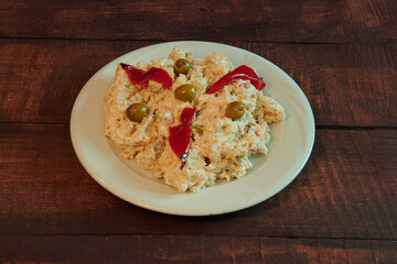 A white plate with a salad on it. The salad has a red pepper and some olives on it