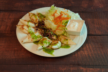 A plate of food with meat and vegetables. The vegetables include carrots and lettuce. The plate is on a wooden table
