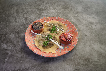 A plate of food with a tortilla on it and a side of beans. There is also a bowl of sauce on the plate