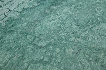 A large green rock with numerous cracks and holes. The rock appears to be made of a material that has been weathered and eroded over time, giving it a rough and textured appearance