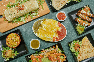 A table with many different types of food, including burritos, enchiladas, and tortillas
