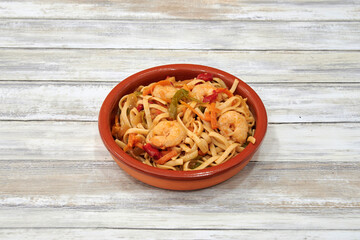 A bowl of food with shrimp and vegetables. The bowl is red and the food is on a white table