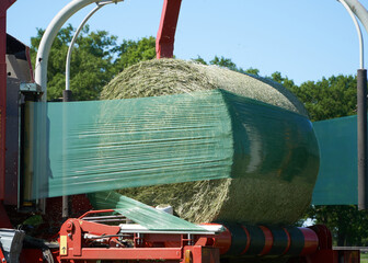 Round bale of hay being tightly wrapped in green silage stretch film