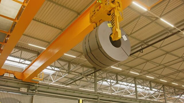 Close up of a crane clamp attached to a overhead bridge picking up a heavy steel coil