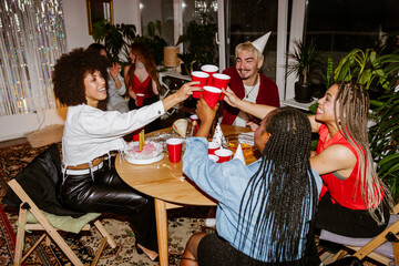 A group of four friends are sitting at a table and laughing while clinking their cups