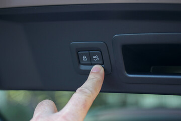 Index finger near the trunk lid closing button of a modern vehicle