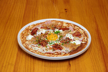 A plate of food with bacon, cheese, and an egg on top. The plate is white and sits on a wooden table