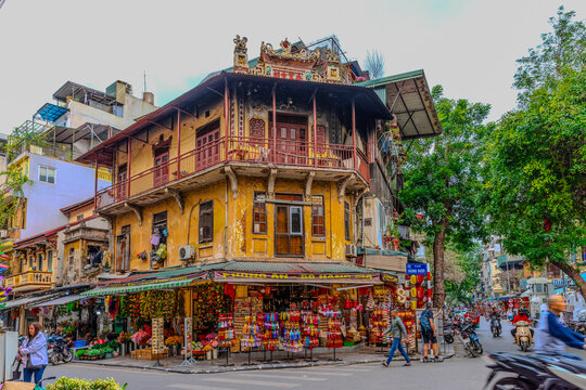 20 March 2025 Hanoi Old Commercial Shops and Apartment house block in Hanoi Old Quarters Vietnam. Trees red bridge and green Pond. Hanoi is bustling with bikes cars and locals and tourists shopping