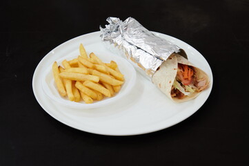 A plate of french fries and a wrap of food is placed on a white plate. The wrap is a burrito, filled with various ingredients such as lettuce, tomatoes, and meat. The fries are golden and crispy