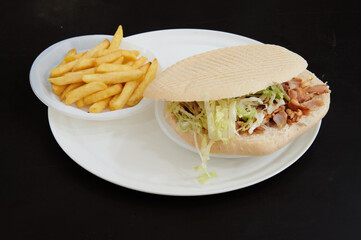 A sandwich with lettuce and meat on a white plate. A side of french fries is on a white plate