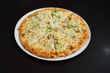 A pizza with cheese and vegetables on it. The pizza is cut into eight slices. It is on a white plate