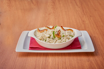A white bowl of rice with green peas and carrots. The bowl is on a red napkin