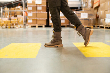 Close-up of the shoes of a warehouse worker walking along a marked walkway in a warehouse.using the marked pedestrian path in the warehouse.Pedestrian safety concept in a warehouse
